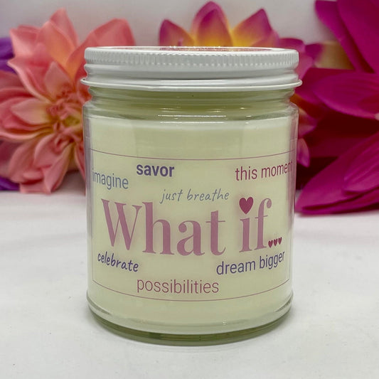 A hand poured candle with label that says What If and other positive words, with white lid and bright floral background.