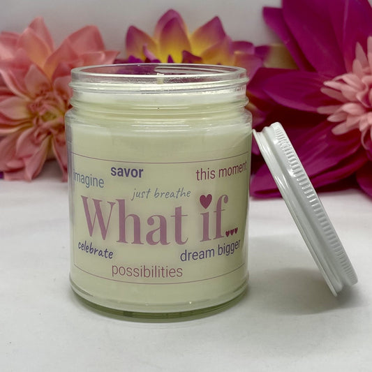 A hand poured candle with label that says What If & other positive words, white lid resting next to it & floral background.