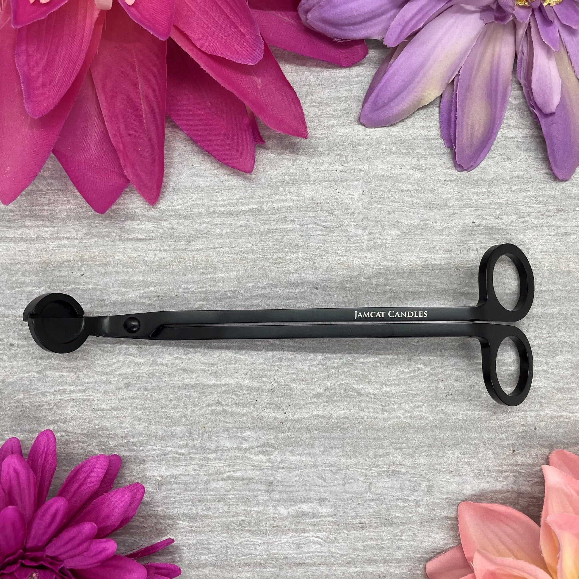 A wick trimmer with a grey background, surrounded by bright, colorful flowers.