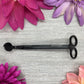 A wick trimmer with a grey background, surrounded by bright, colorful flowers.