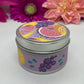 Hand poured candle in silver tin with colorful fruit label on lid and body of the tin, with bright floral background.