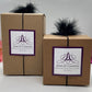 Kraft gift boxes in 2 sizes decorated with a Jamcat Candles logo card and black feather puff elastic.